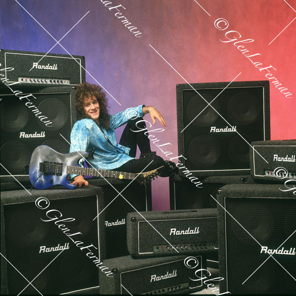 Vivian Campbell in studio leaning back on amps, smiling