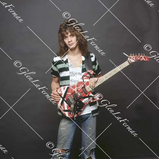 Eddie Van Halen in striped shirt and Kramer Frankenstrat serious with grey backdrop